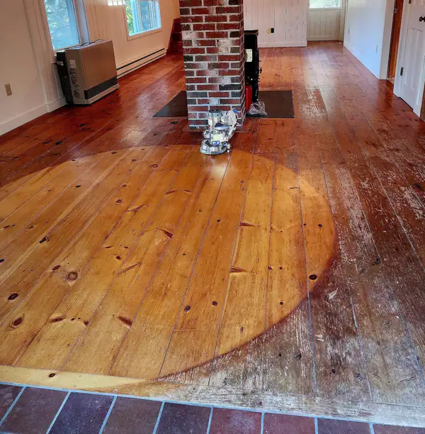 Wide pine floor before: old orange finish worn through around a brick chimney