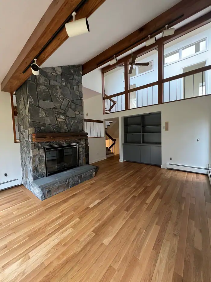Light oak floor running to a stone fireplace under exposed beams