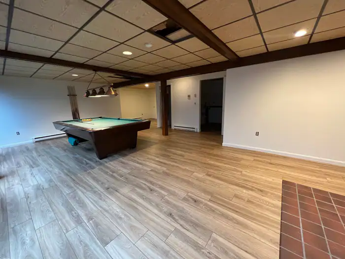 Plank floor through a basement with exposed beams and a brick hearth