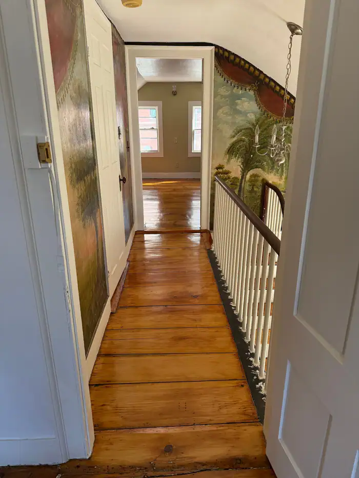 Wide pine boards down a hallway beside a white railing