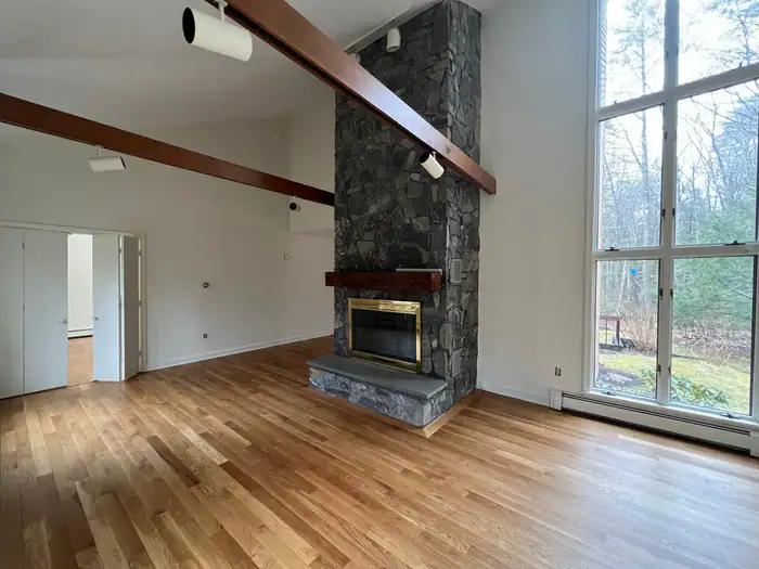 Oak floor and stone fireplace in a tall room with a wall of windows