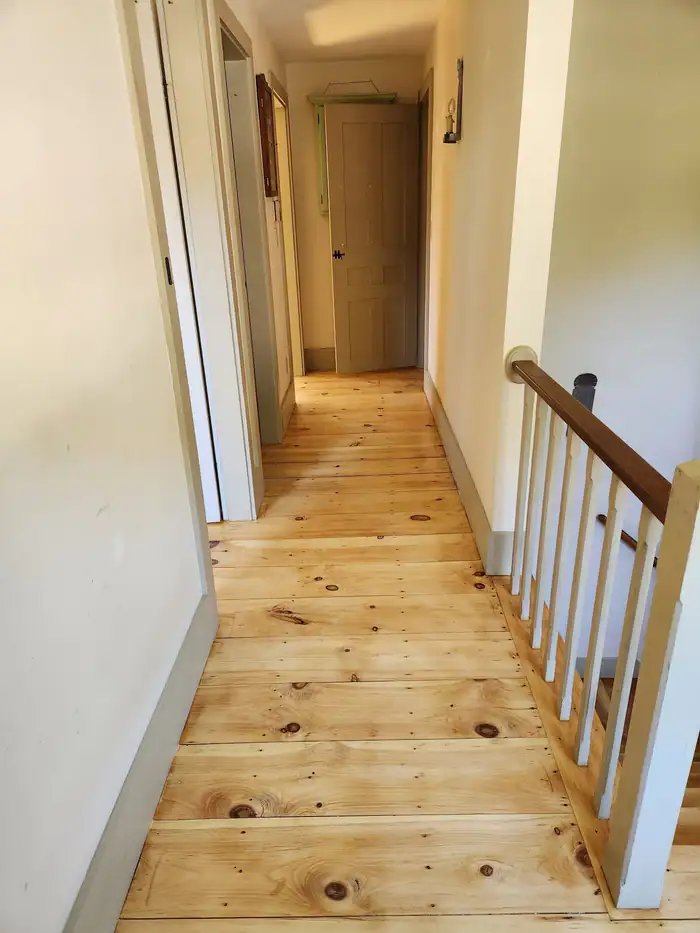Pine hallway floor beside a white stair railing
