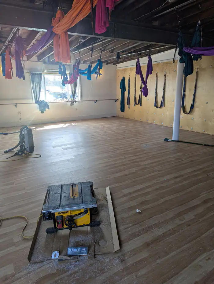 Studio floor mid-install with a table saw and aerial silks overhead