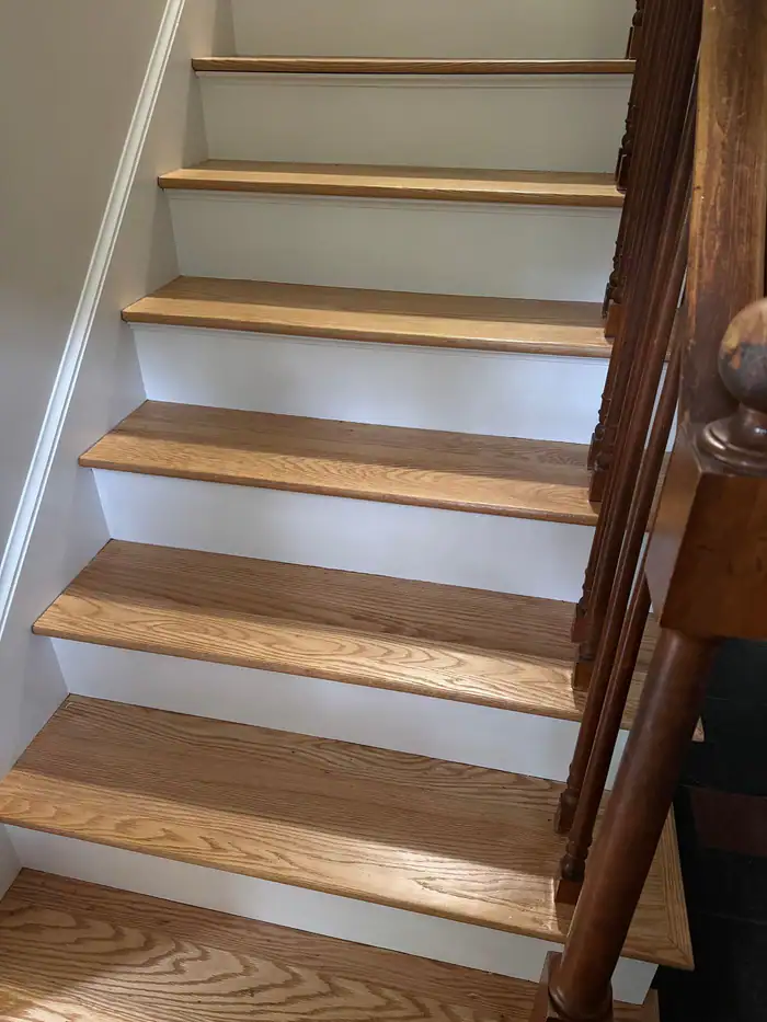 Oak stair treads over white risers beside a dark wood railing