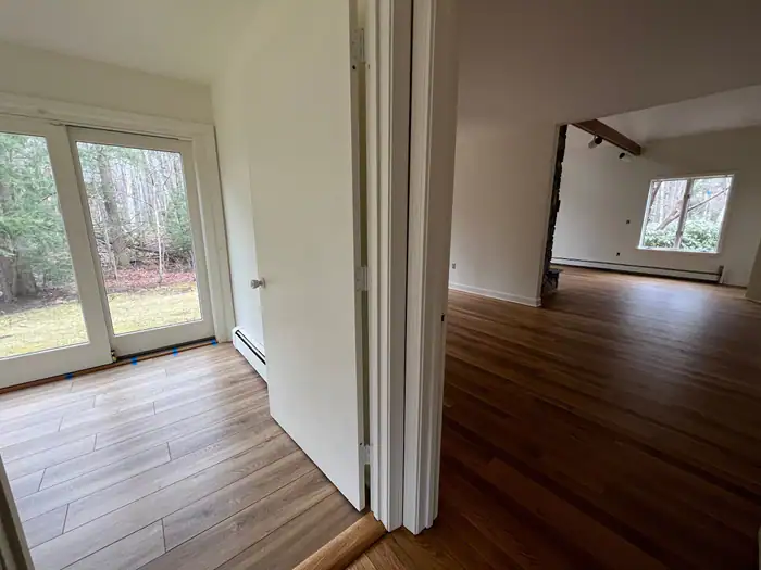 Plank floor through a doorway into a bright room with patio doors