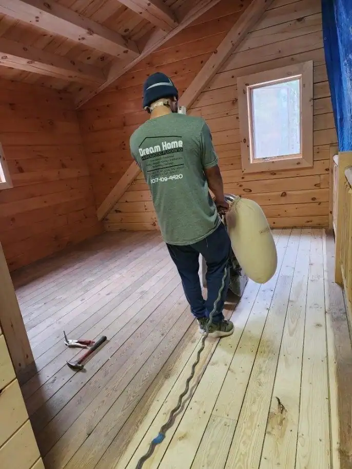 Dream Home crew member in a company shirt sanding a pine floor in a knotty-pine room