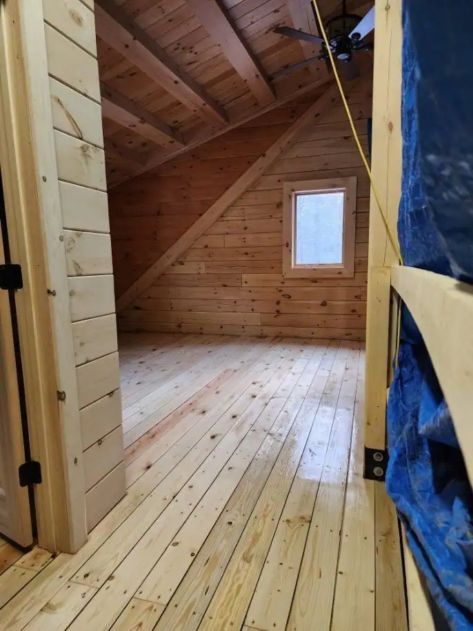 Crew member sanding pine boards in a knotty-pine cabin room