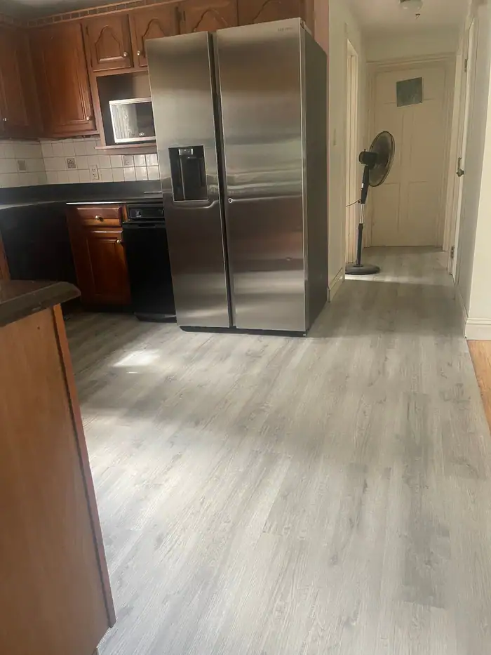 Gray plank floor laid through a kitchen with a stainless refrigerator